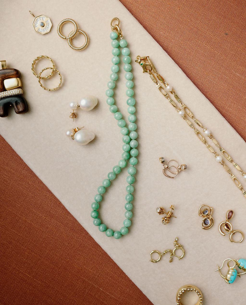 Collection of fine jewelry, made of yellow gold, gemstones, pearls, and wood, like necklaces and earrings on a two-tone fabric background